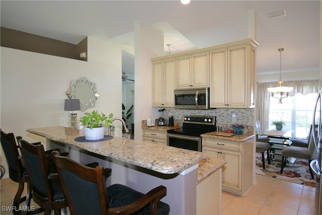 kitchen with appliances with stainless steel finishes, a breakfast bar, pendant lighting, and cream cabinets