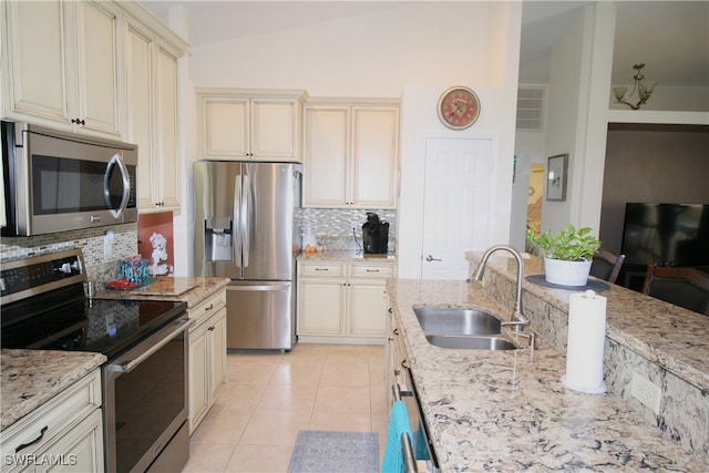 kitchen with appliances with stainless steel finishes, sink, cream cabinets, backsplash, and lofted ceiling