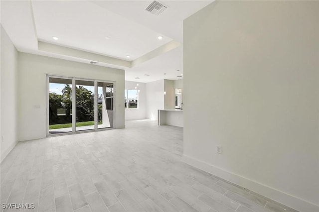 unfurnished room with a tray ceiling, recessed lighting, visible vents, and light wood-style floors