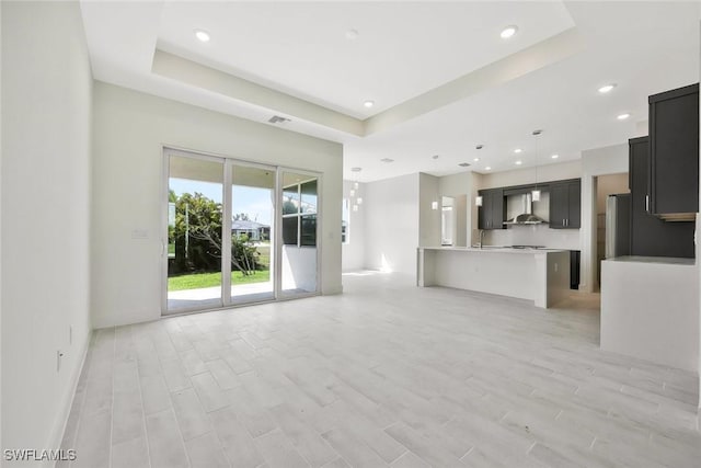 unfurnished living room with light wood-style flooring, visible vents, a tray ceiling, and recessed lighting