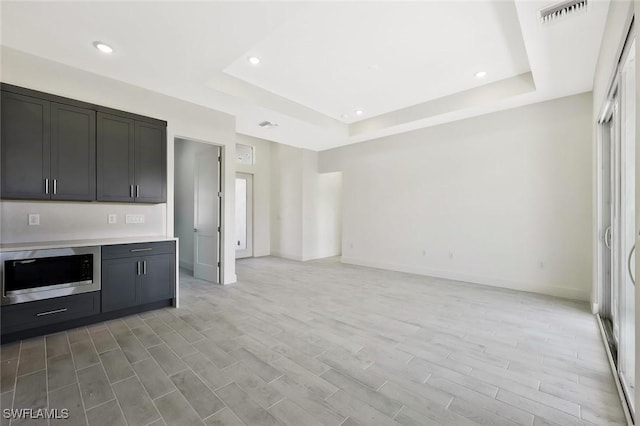 kitchen with visible vents, light wood-style floors, light countertops, a tray ceiling, and stainless steel microwave