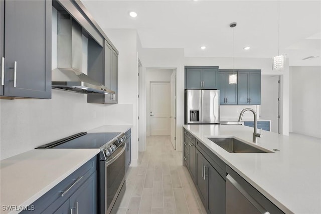 kitchen with a sink, light countertops, appliances with stainless steel finishes, and wall chimney range hood