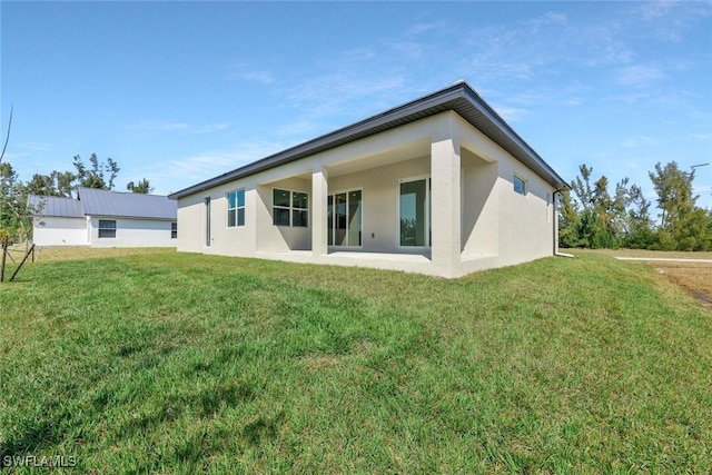 back of house with stucco siding and a yard