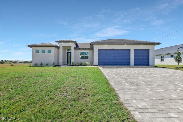 prairie-style home featuring a front lawn, decorative driveway, an attached garage, and stucco siding