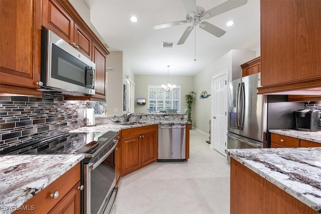 kitchen with brown cabinetry, backsplash, light stone counters, ceiling fan with notable chandelier, and stainless steel appliances