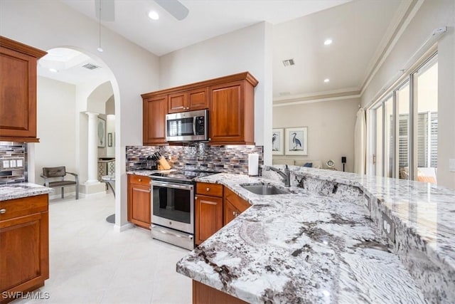 kitchen with ceiling fan, appliances with stainless steel finishes, arched walkways, light stone countertops, and a sink
