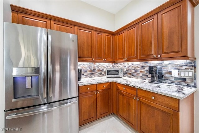 kitchen with light stone counters, brown cabinetry, decorative backsplash, a toaster, and stainless steel refrigerator with ice dispenser