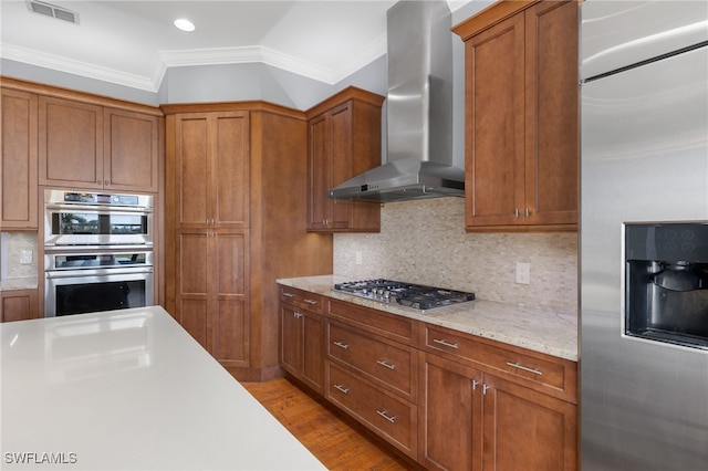 kitchen with stainless steel appliances, decorative backsplash, wall chimney exhaust hood, crown molding, and light wood-type flooring