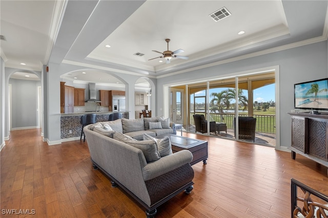 living room with hardwood / wood-style floors, ceiling fan, a raised ceiling, and crown molding