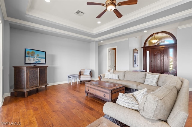 living room with ornamental molding, wood-type flooring, ceiling fan, and a raised ceiling