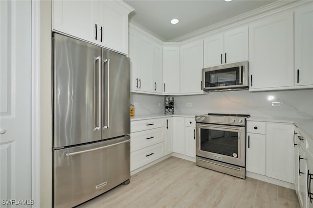 kitchen with ornamental molding, appliances with stainless steel finishes, light stone counters, and white cabinetry