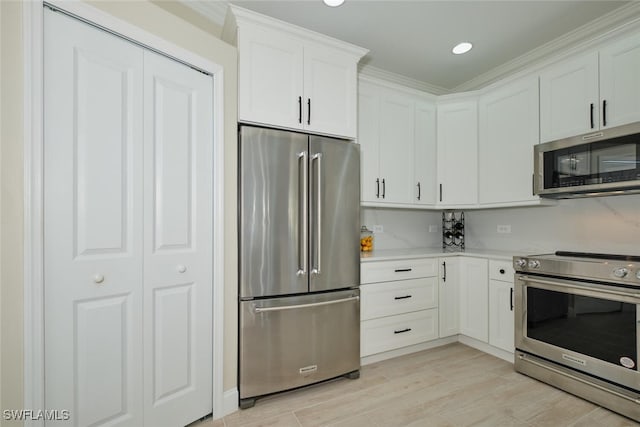 kitchen with appliances with stainless steel finishes, ornamental molding, white cabinets, and light hardwood / wood-style floors