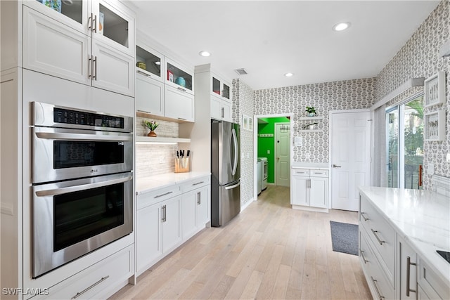 kitchen with white cabinets, light wood-type flooring, light stone countertops, appliances with stainless steel finishes, and tasteful backsplash