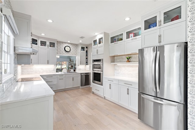 kitchen featuring appliances with stainless steel finishes, tasteful backsplash, light stone counters, light hardwood / wood-style floors, and white cabinetry