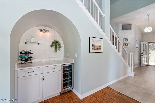 bar featuring white cabinets, decorative light fixtures, high vaulted ceiling, and beverage cooler