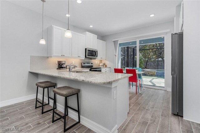 kitchen featuring decorative backsplash, appliances with stainless steel finishes, wood tiled floor, white cabinetry, and a sink