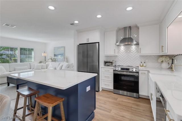 kitchen featuring appliances with stainless steel finishes, wall chimney range hood, light hardwood / wood-style flooring, and white cabinetry