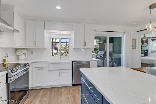 kitchen with white cabinetry, light hardwood / wood-style floors, stainless steel appliances, decorative light fixtures, and blue cabinetry