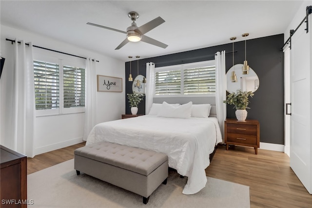 bedroom featuring a barn door, wood-type flooring, and ceiling fan