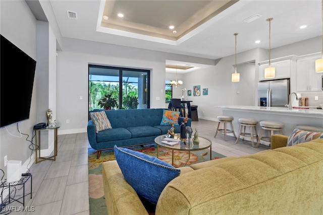 living room with a tray ceiling, an inviting chandelier, and sink