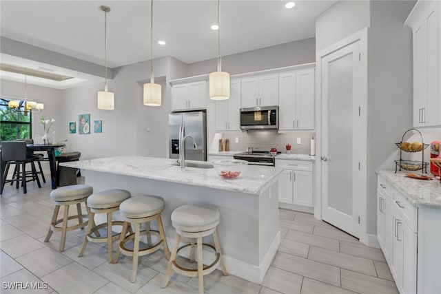 kitchen with white cabinets, decorative light fixtures, light stone counters, and stainless steel appliances