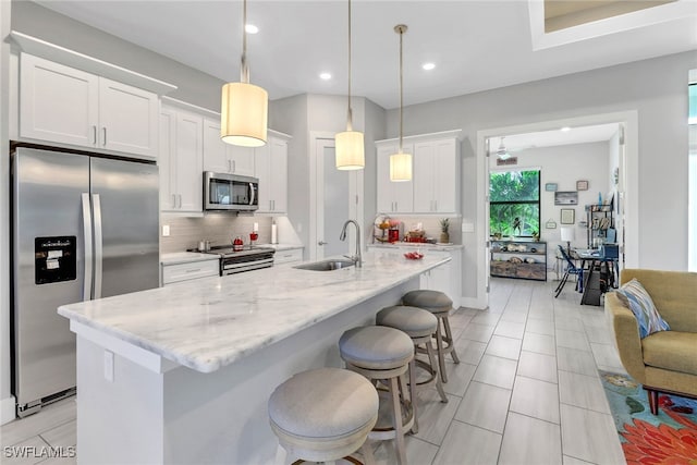 kitchen featuring light stone countertops, tasteful backsplash, stainless steel appliances, decorative light fixtures, and white cabinetry