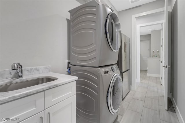 laundry area featuring cabinets, stacked washing maching and dryer, and sink