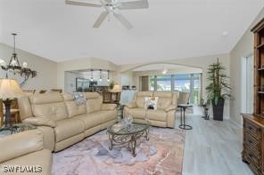 living room featuring vaulted ceiling, light wood-type flooring, and ceiling fan with notable chandelier