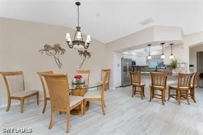 dining area featuring a notable chandelier, light wood-type flooring, and vaulted ceiling