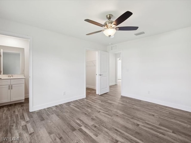 unfurnished bedroom with a closet, ensuite bath, a spacious closet, light hardwood / wood-style floors, and ceiling fan