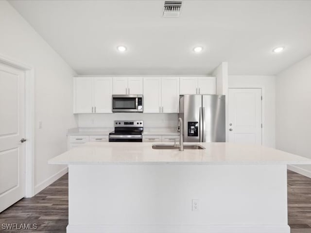 kitchen with dark hardwood / wood-style flooring, appliances with stainless steel finishes, white cabinetry, and an island with sink