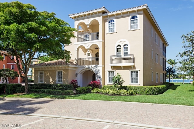 mediterranean / spanish-style home featuring a tile roof, a balcony, a front lawn, and stucco siding