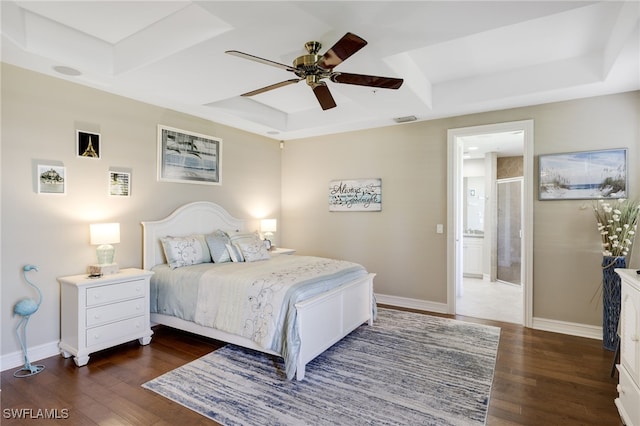 bedroom featuring ensuite bath, dark wood-type flooring, a raised ceiling, and ceiling fan