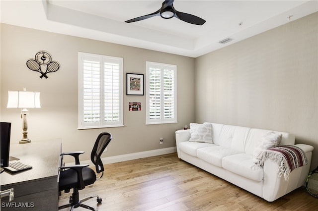 home office with light hardwood / wood-style flooring, a raised ceiling, and ceiling fan