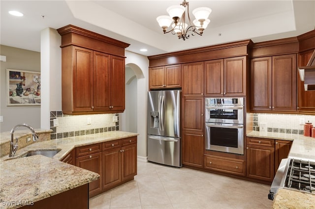 kitchen with stainless steel appliances, backsplash, sink, light stone countertops, and decorative light fixtures