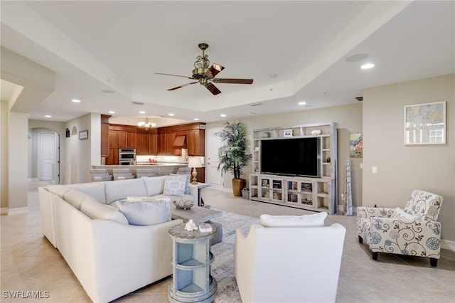 living room with light tile patterned flooring, a tray ceiling, and ceiling fan with notable chandelier