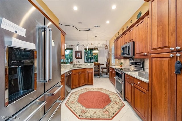 kitchen with light stone countertops, decorative light fixtures, stainless steel appliances, sink, and light tile patterned floors