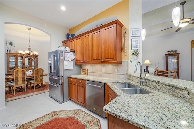 kitchen featuring sink, stainless steel appliances, light tile patterned floors, light stone counters, and ceiling fan with notable chandelier