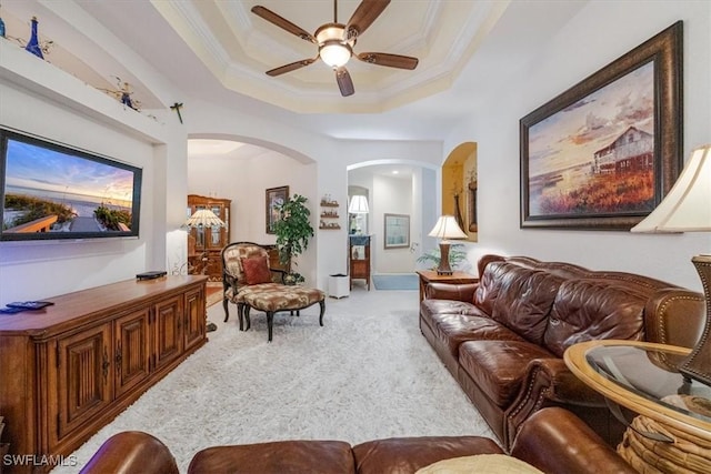 carpeted living room with a raised ceiling, ceiling fan, and ornamental molding