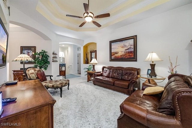 carpeted living room featuring ceiling fan, ornamental molding, and a raised ceiling