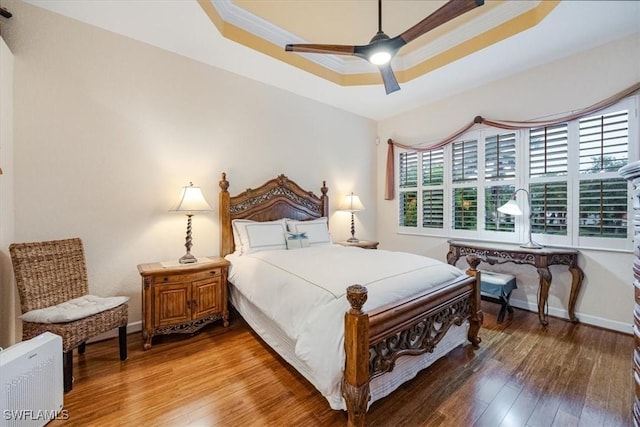 bedroom with ceiling fan, wood-type flooring, and a raised ceiling