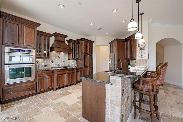 2546 Marquesa Royale Ln Unit 7-302, Naples, FL 34109 - kitchen featuring premium range hood, arched walkways, stone tile flooring, appliances with stainless steel finishes, and dark stone countertops