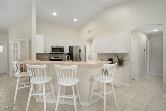 kitchen with light tile patterned floors, appliances with stainless steel finishes, a kitchen breakfast bar, white cabinetry, and high vaulted ceiling