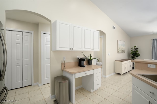 kitchen with white cabinetry, vaulted ceiling, light tile patterned floors, and sink