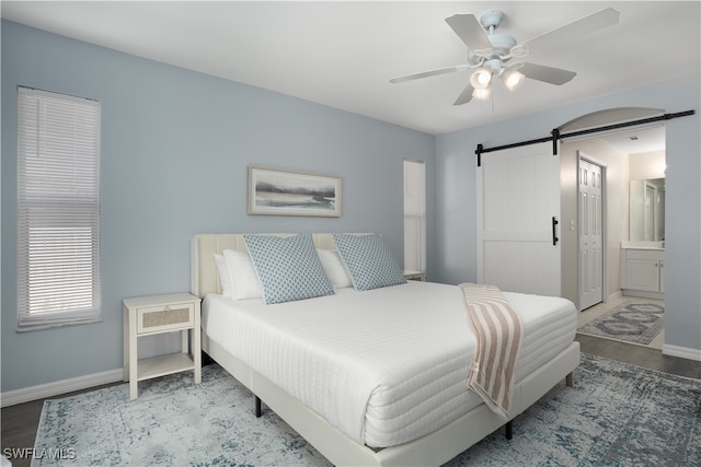 bedroom featuring connected bathroom, a barn door, and ceiling fan