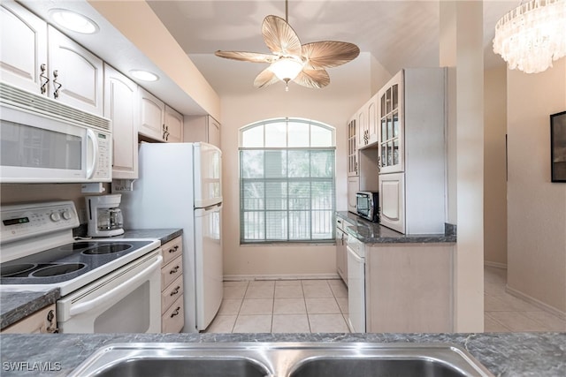 kitchen with light tile patterned flooring, ceiling fan with notable chandelier, white appliances, and white cabinets