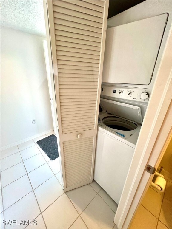 laundry room with a textured ceiling, light tile patterned flooring, and stacked washer and clothes dryer