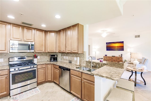 kitchen with a breakfast bar area, kitchen peninsula, stainless steel appliances, light stone countertops, and tasteful backsplash