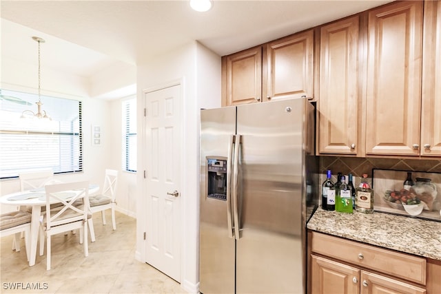 kitchen with hanging light fixtures, stainless steel fridge, light stone countertops, a notable chandelier, and tasteful backsplash