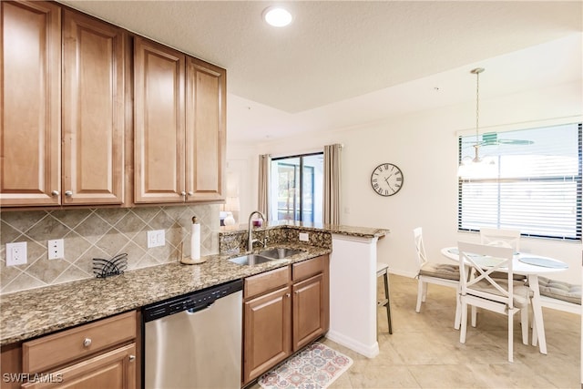 kitchen featuring hanging light fixtures, backsplash, sink, stainless steel dishwasher, and stone counters